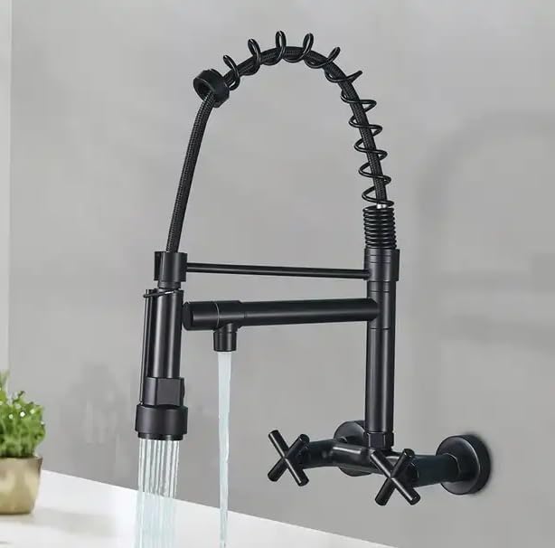 A matte black wall-mounted kitchen faucet with a flexible spring-loaded gooseneck sprayer, cross-handle valves, and running water, shown against a light gray wall.